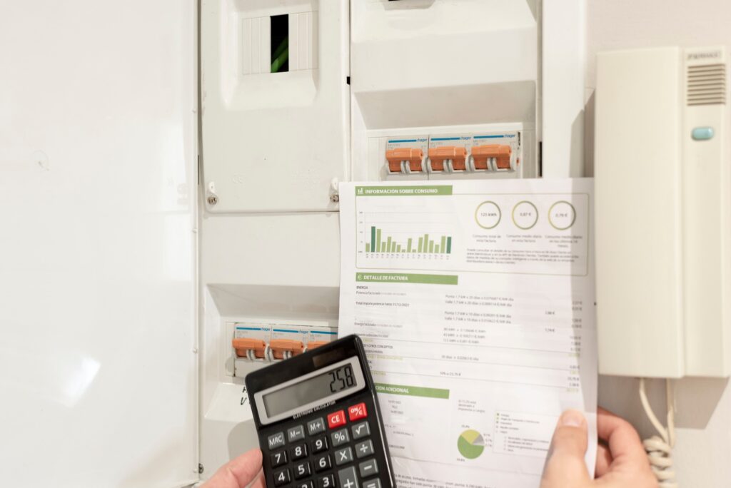 a hand holding an electricity bill and calculator in front of power control switch